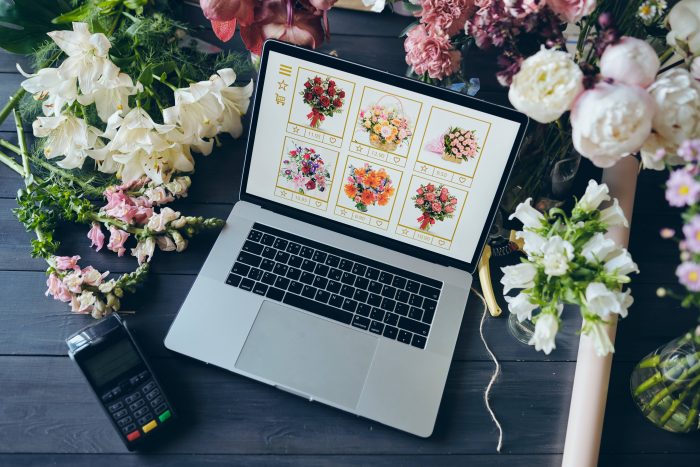 Business owner's laptop. Florist website on a laptop screen on a table covered with flowers. 